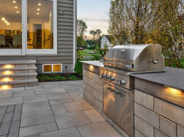 An outdoor kitchen with a stainless teel grill on a stone patio