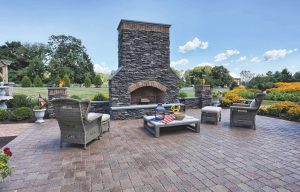 A stone patio with an outdoor fireplace in the center surrounded by chairs