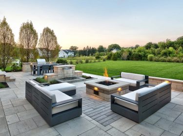 A hardscape patio with a fire pit in the center, surrounded by chairs