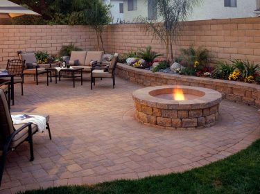 A hardscape patio with a table and chairs placed next to a fire pit