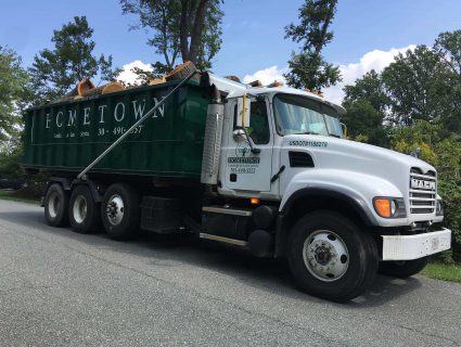 A flat bed truck transporting a roll-off dumpster